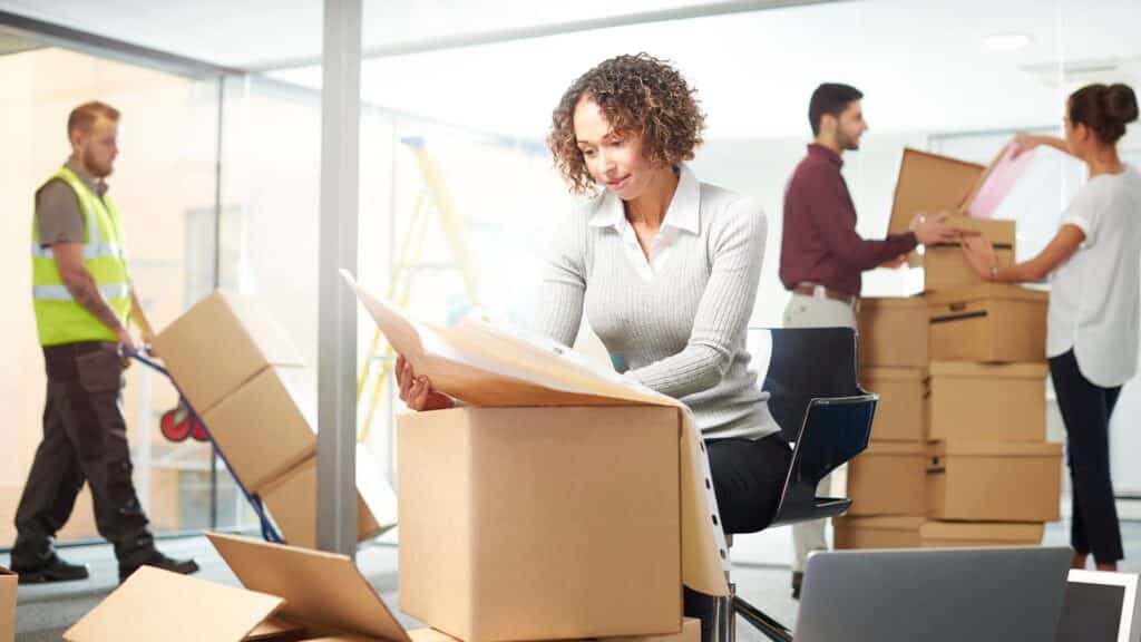 Professional office move in progress: a businesswoman reviews documents while movers transport boxes and employees organize belongings, showcasing the do's and don'ts of moving your office and highlighting Abe Lincoln Movers’ expertise in seamless commercial relocations.