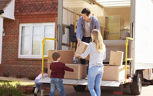 Family unloading boxes from a large moving truck together.