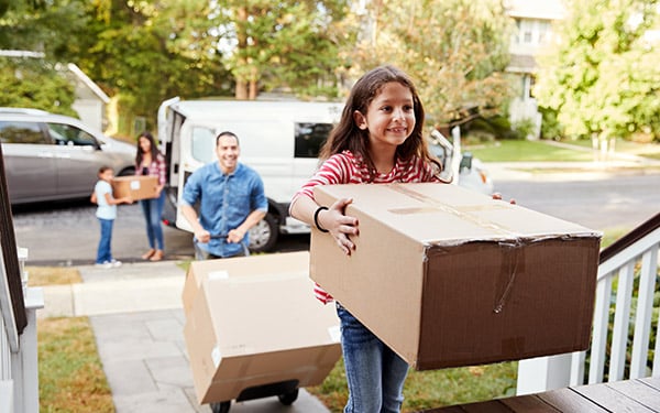 Little girl carrying a cardboard box into her new home.