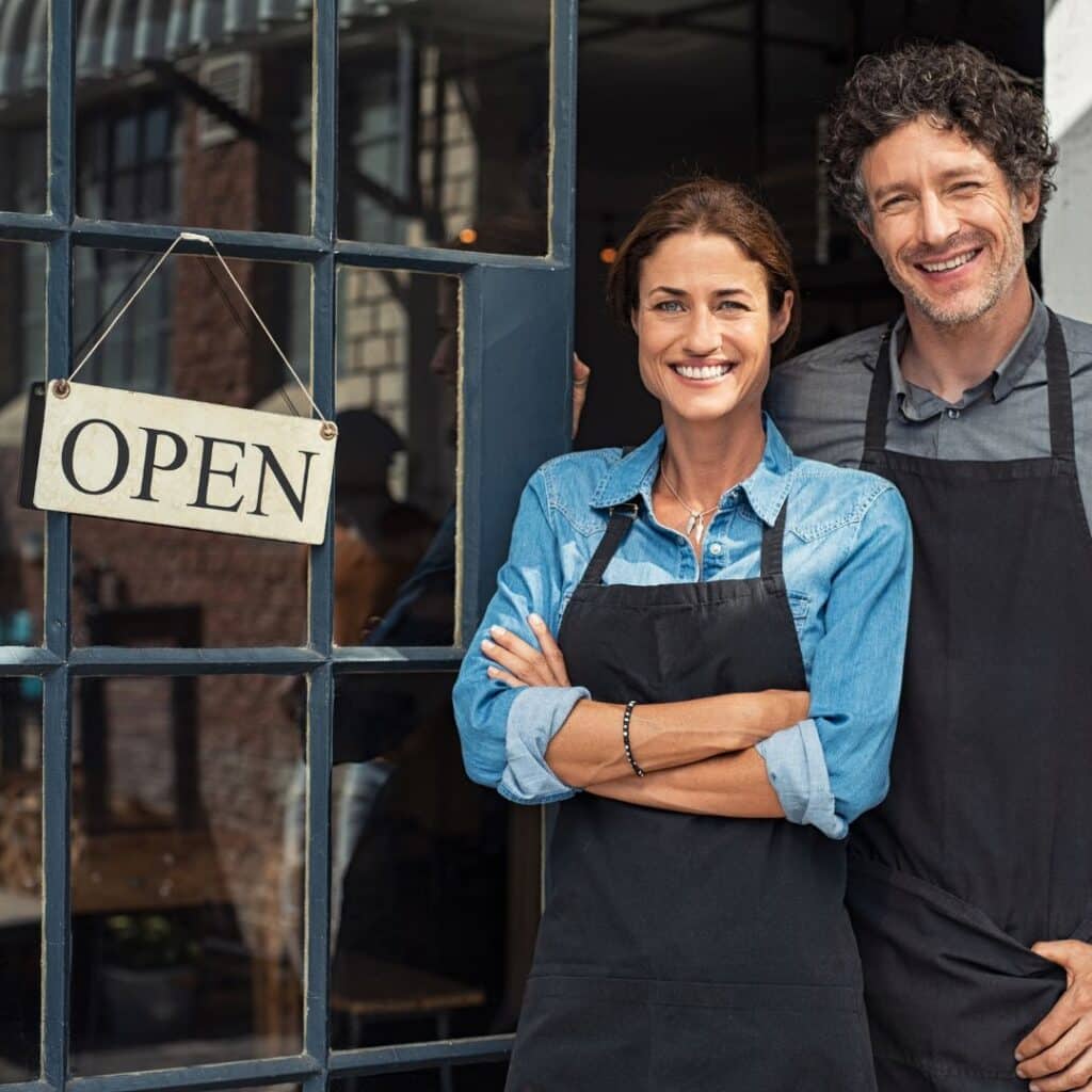 small business owners standing next to an open sign celebrating a successful small business move 