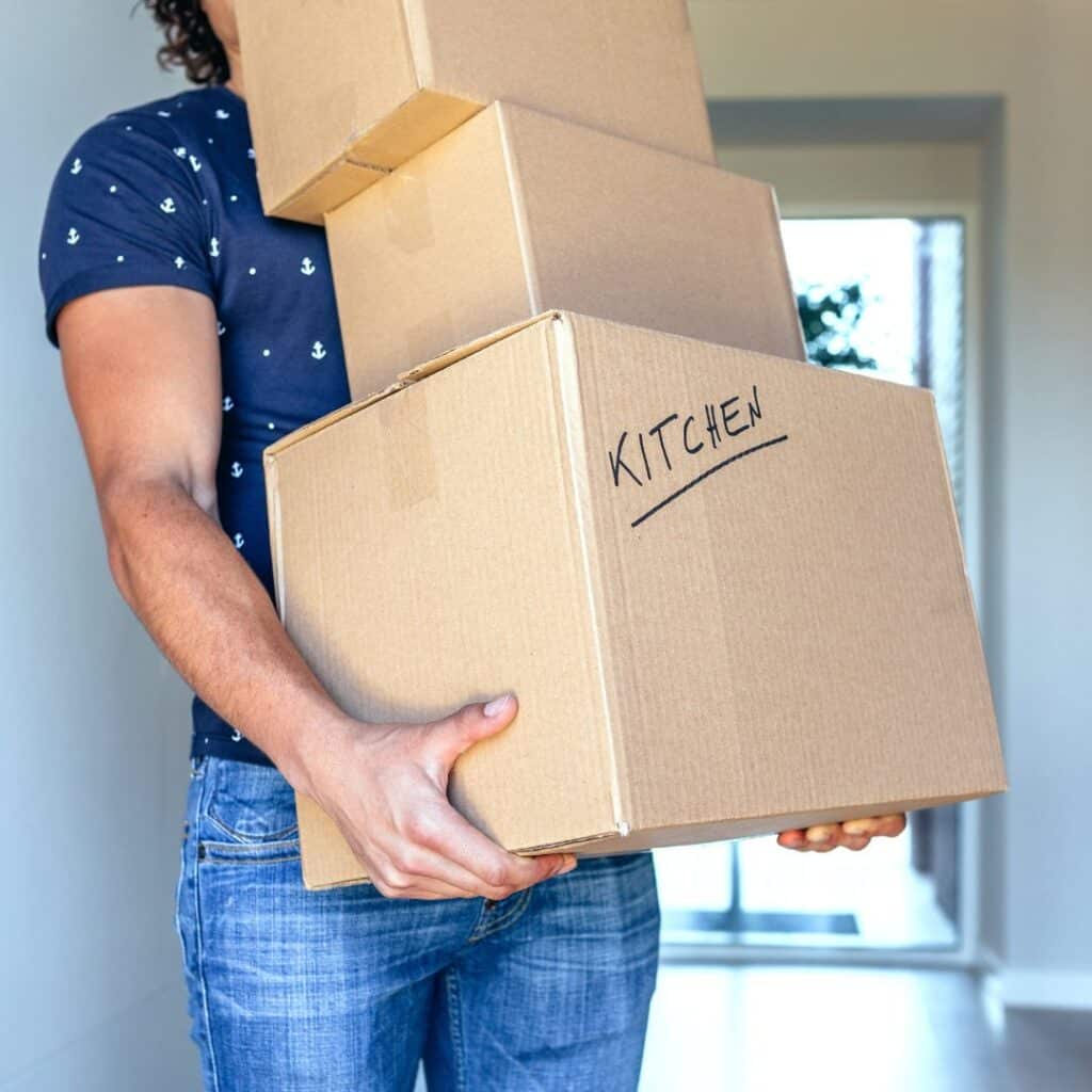 A man carrying moving boxes labeled by room