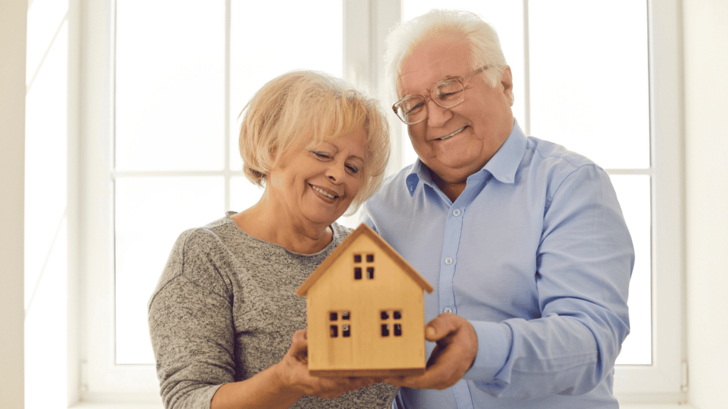 A senior couple holding a small, wooden model of a house to represent senior moving