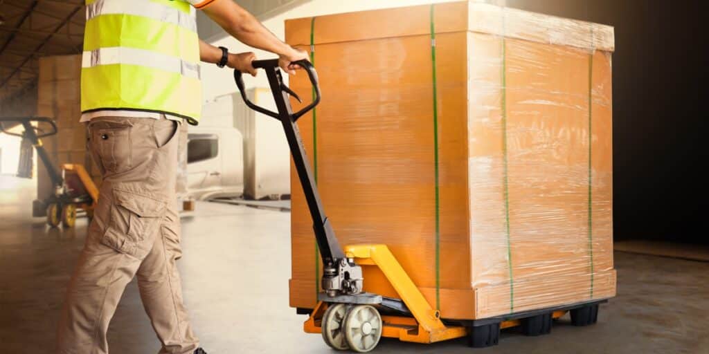 Professional mover in a safety vest using a pallet jack to transport a securely wrapped and strapped large box in a well-lit warehouse, showcasing specialty moving services.