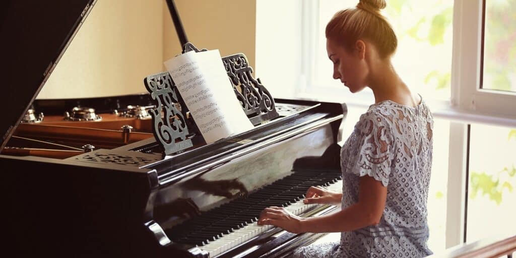 Close-up of a grand piano being played by a woman in a bright, serene room, emphasizing the precision and care required in piano transport by professional movers to preserve its beauty and functionality.