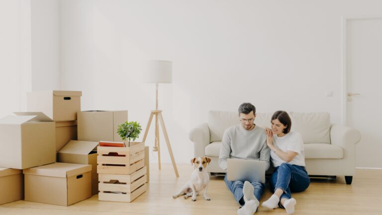 Couple sitting on the floor with moving boxes and a dog while preparing to move out of their rental in Denver.