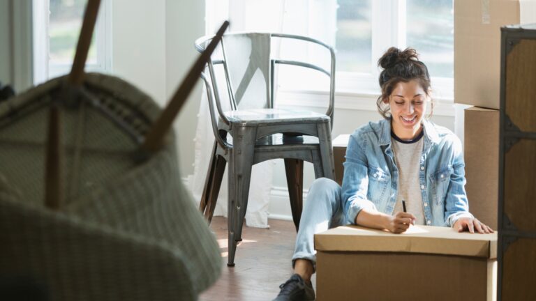 Young woman labeling boxes during a move, following apartment moving tips to stay organized in her Denver rental.