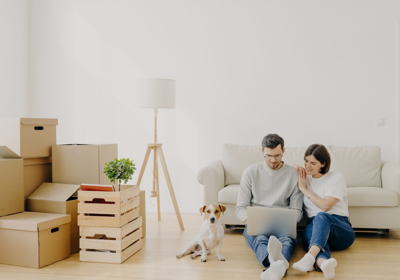 Couple sitting on the floor with moving boxes and a dog while preparing to move out of their rental in Denver.