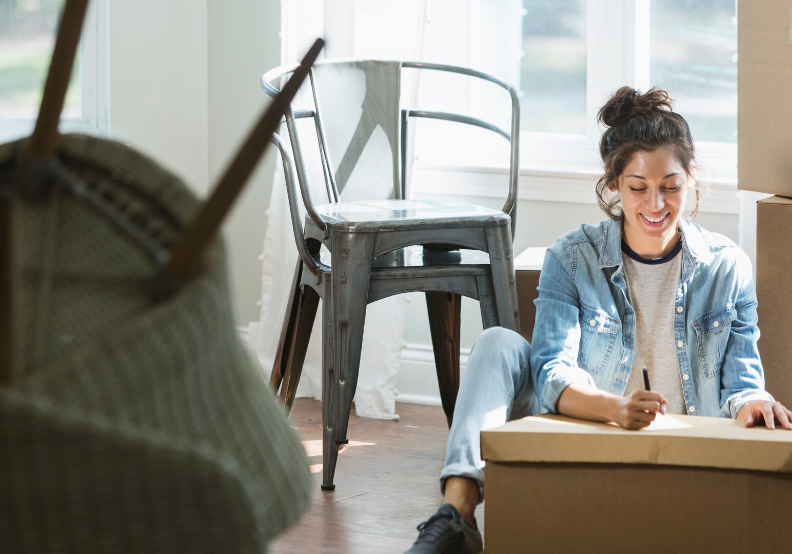 Young woman labeling boxes during a move, following apartment moving tips to stay organized in her Denver rental.