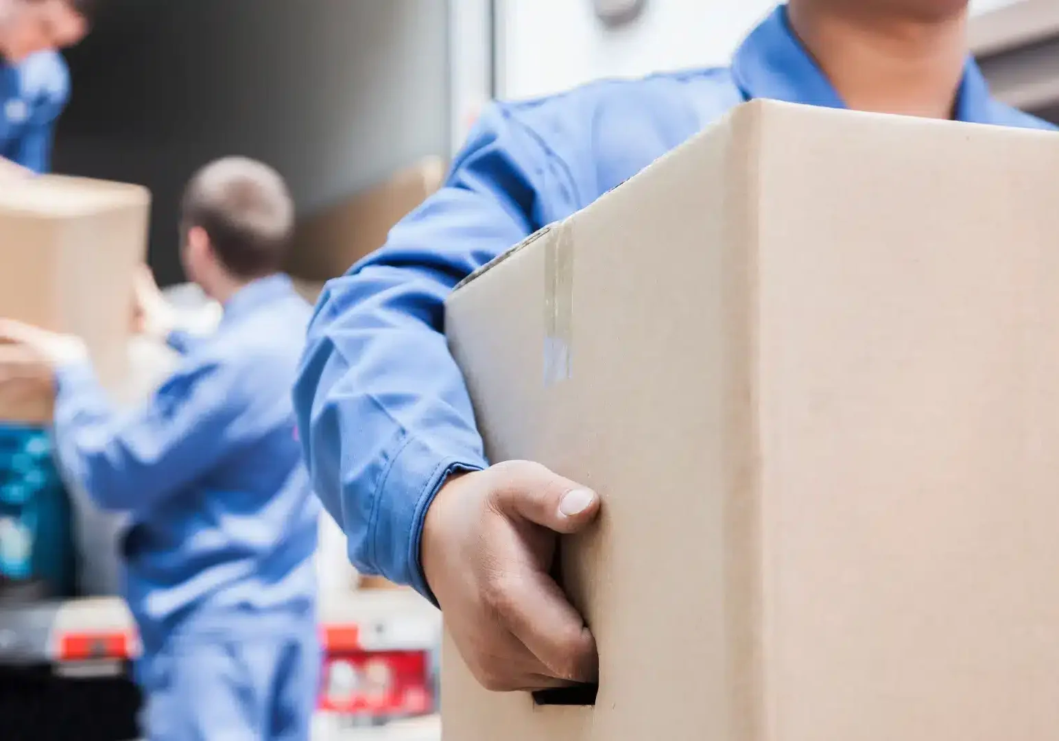 Professional movers in blue uniforms carefully carrying moving boxes during residential relocation service