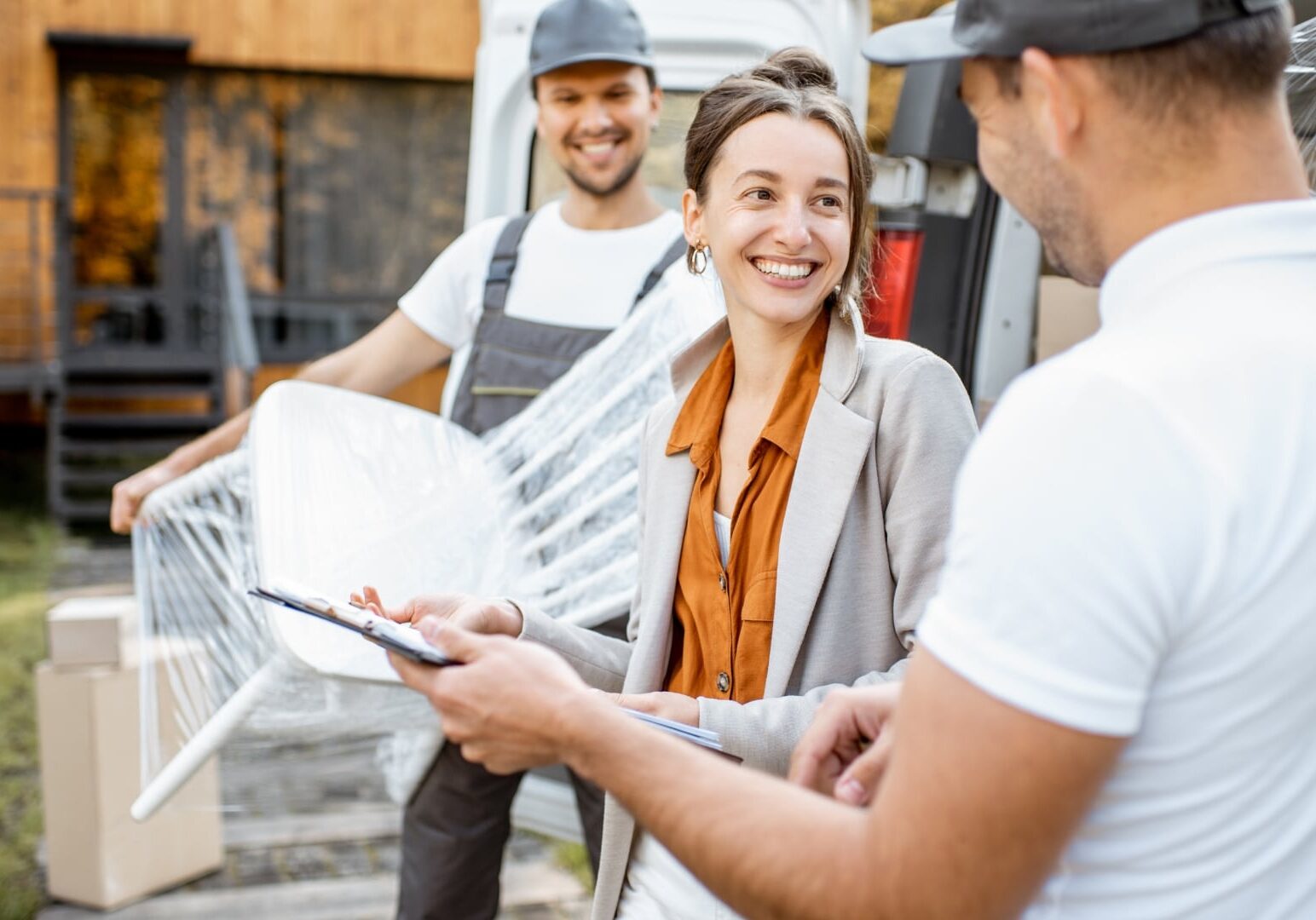 Professional movers assisting a smiling client with specialty moving services, carefully handling packed furniture and household items outdoors.